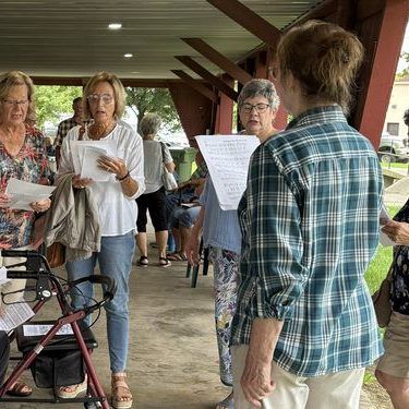 Singers gathered with hymnals under the pavilion