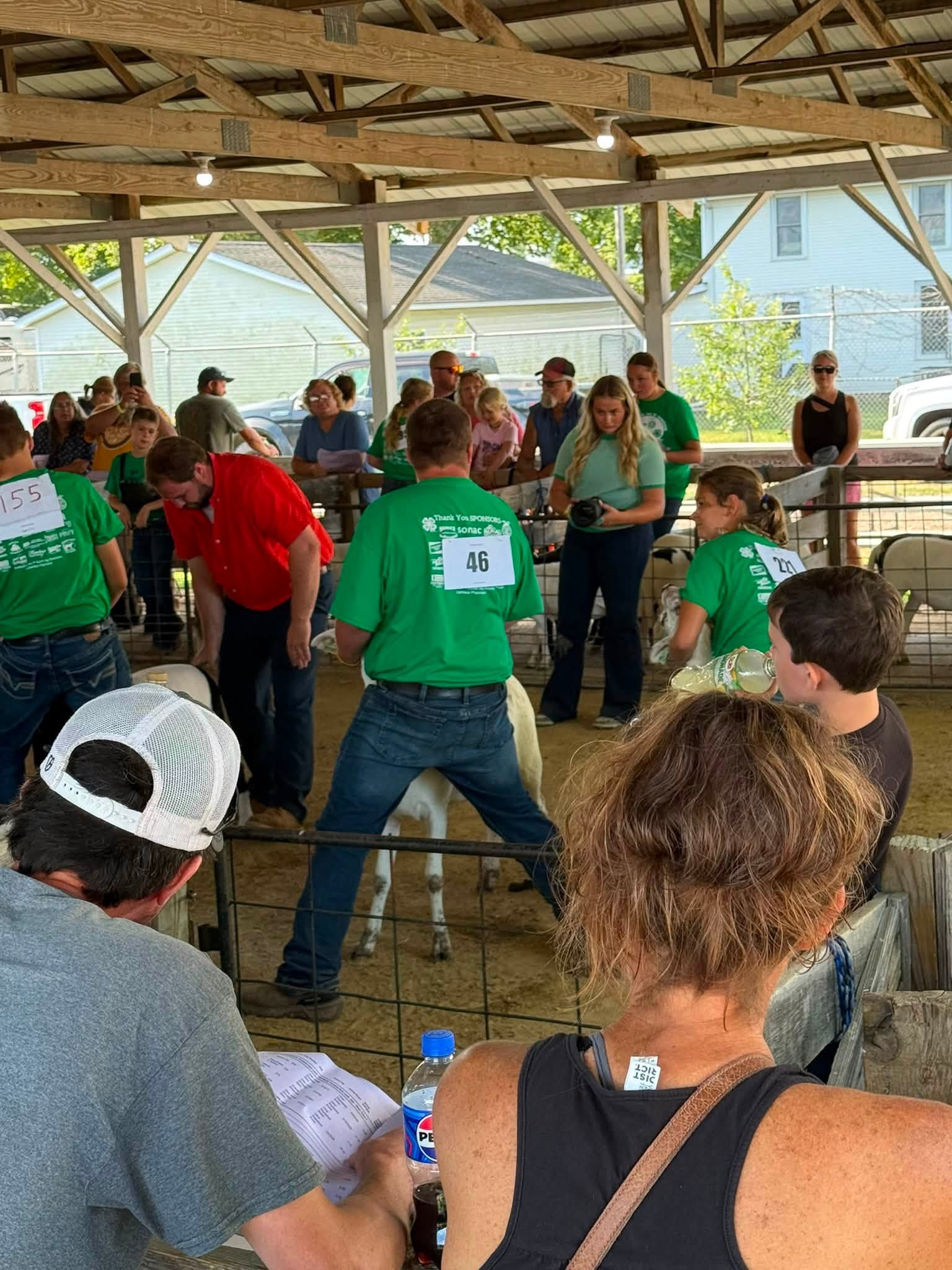 Exhibitors in green shirts and a crowd gather in a covered show arena.