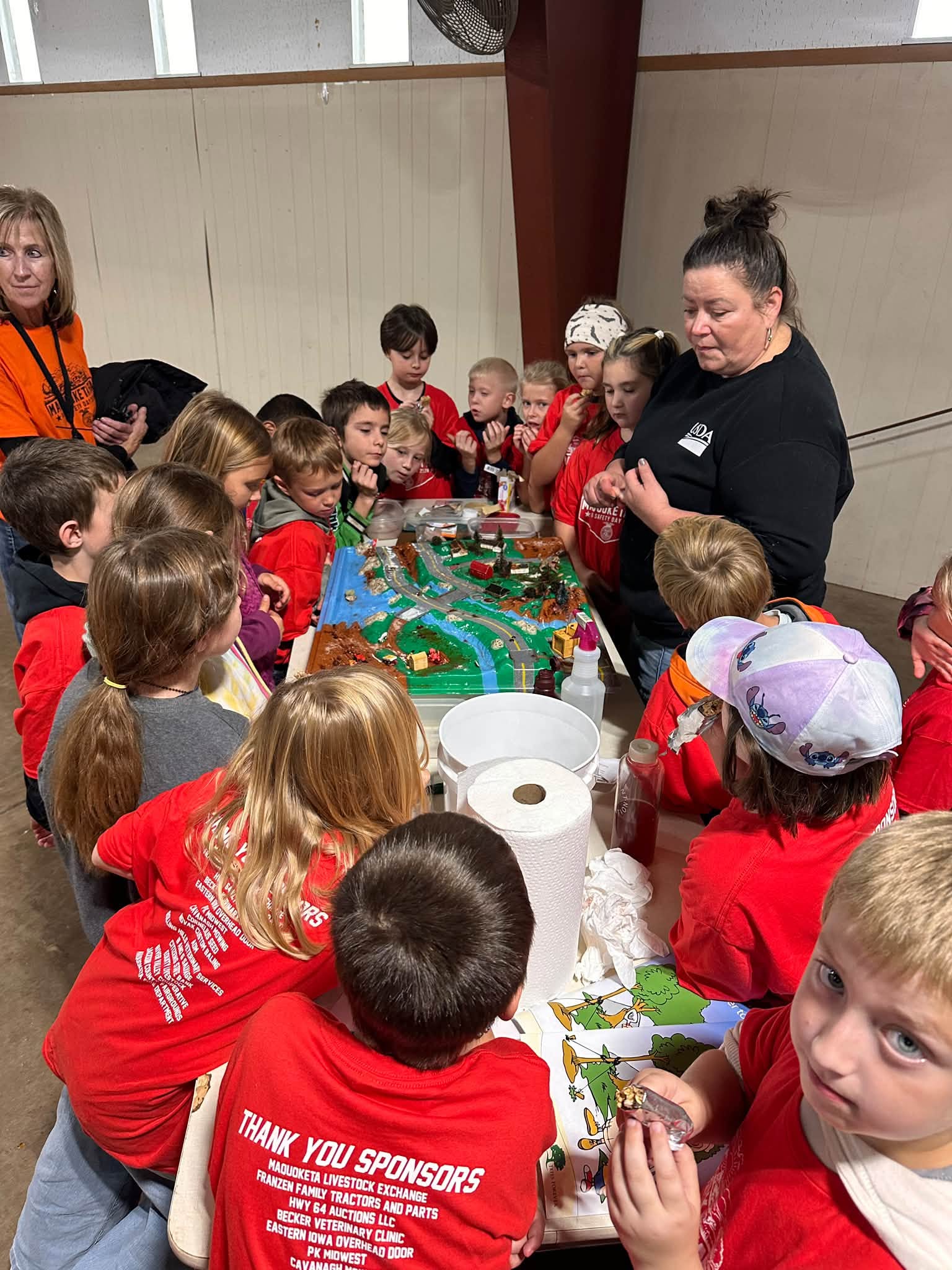 Children in red shirts at a table doing a hands-on activity with an FFA member.