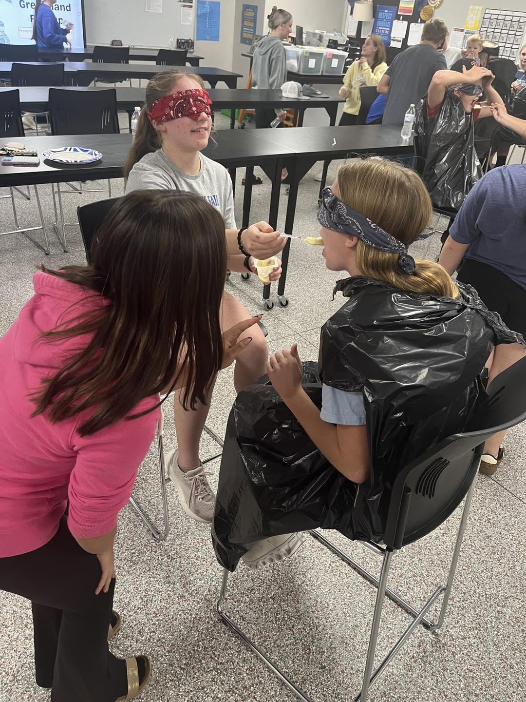 A blindfolded student wearing a trash bag poncho takes part in a game.