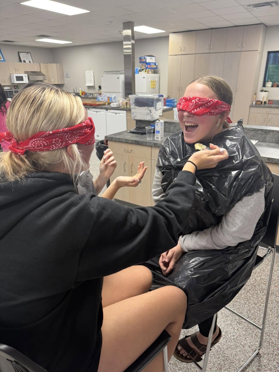 A blindfolded student with a red bandana being helped by a partner during a game.
