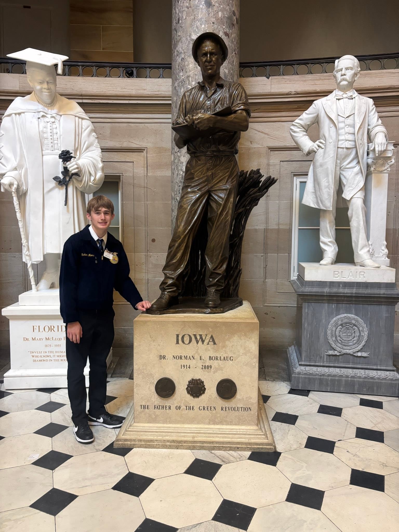 A member in an FFA jacket stands beside a bronze statue with an Iowa plaque.
