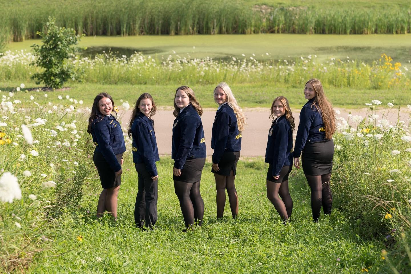 The six officers in blue FFA jackets standing in a meadow of white wildflowers.