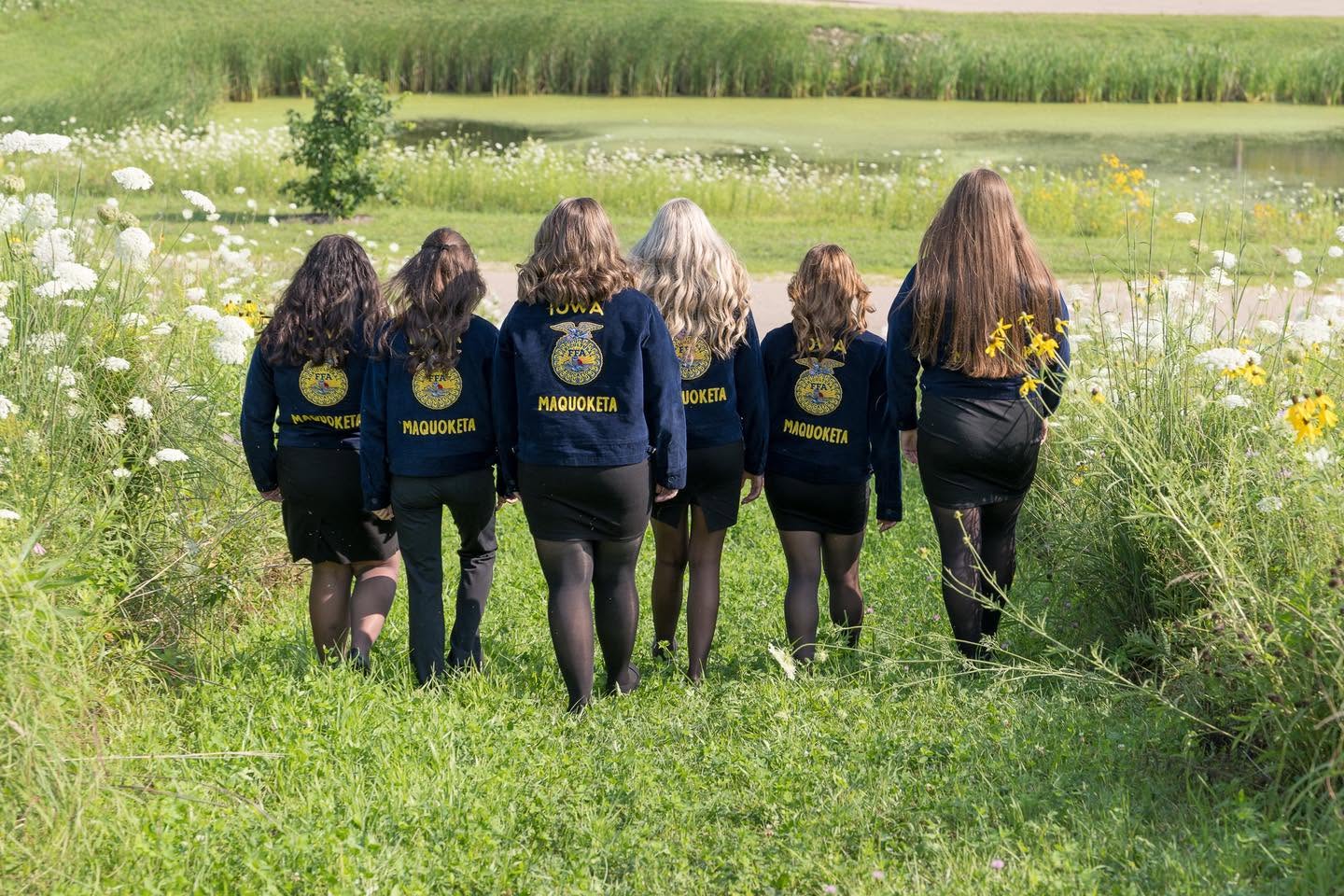 The six officers walk away through tall grass, with FFA lettering on the backs of their jackets.