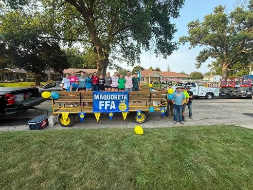 The Maquoketa FFA float, a flatbed wagon with a blue banner and balloons, stopped on a street.