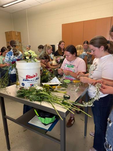 Members arranging flowers around a long work table.