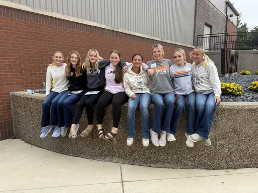 Members sitting along a low stone wall beside potted mums.