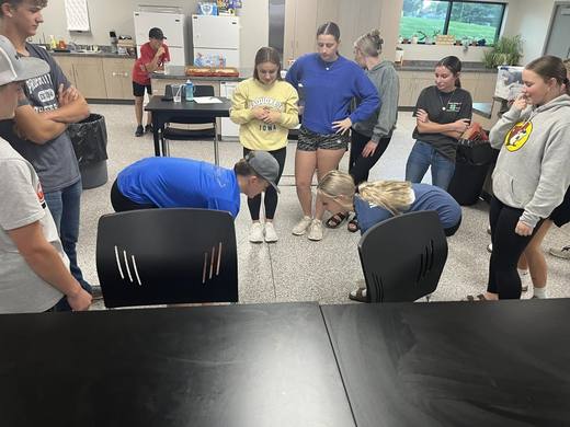Members and Greenhand students gathered around tables in a classroom for a game.