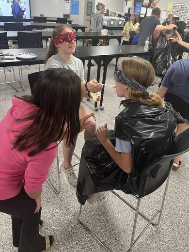 A blindfolded student wearing a trash bag poncho takes part in a game.