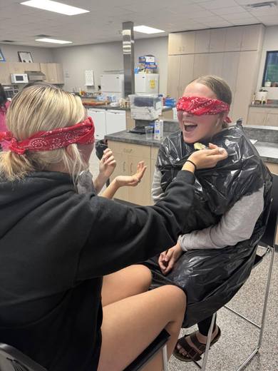 A blindfolded student with a red bandana being helped by a partner during a game.