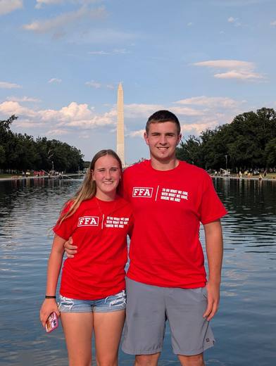 Two members in red FFA shirts stand in front of the Washington Monument and reflecting pool.