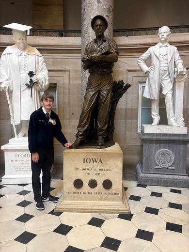 A member in an FFA jacket stands beside a bronze statue with an Iowa plaque.