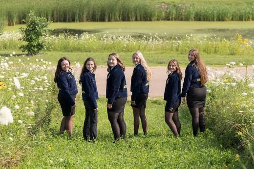 The six officers in blue FFA jackets standing in a meadow of white wildflowers.