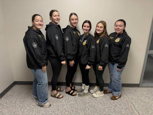 The six officers in black chapter jackets stand against a wall.