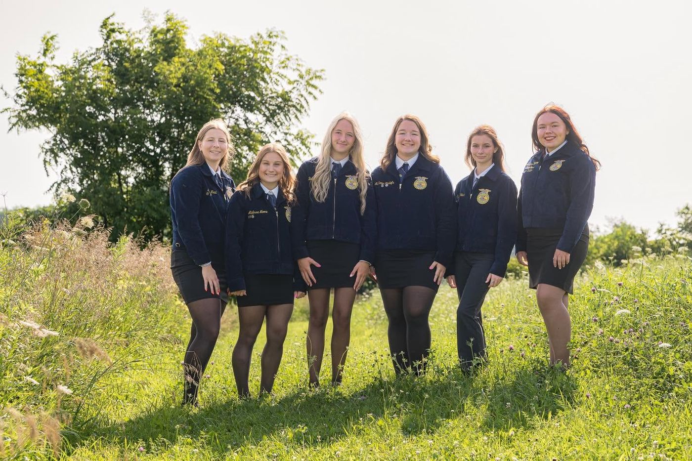 The six 2026-2027 Maquoketa FFA officers standing together in blue FFA jackets in a field of wildflowers.