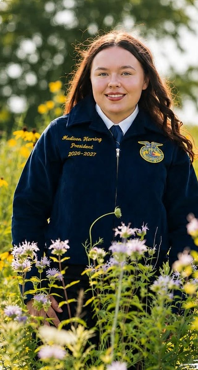 Madison Herring in her FFA jacket, standing in a field of wildflowers.