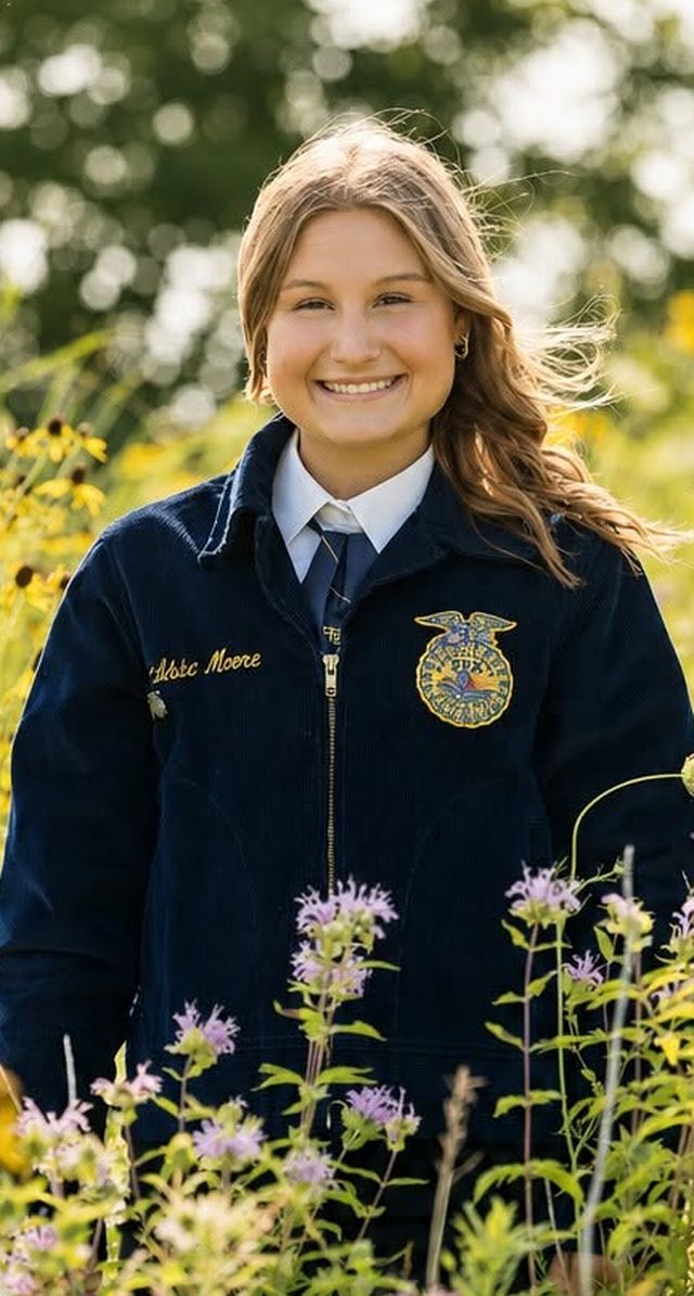 Atty Moore in her FFA jacket, standing in a field of wildflowers.