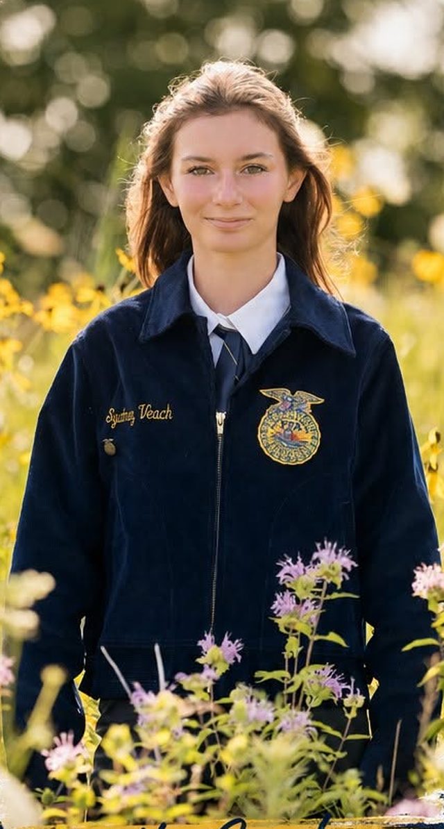 Sydney Veach in her FFA jacket, standing in a field of wildflowers.